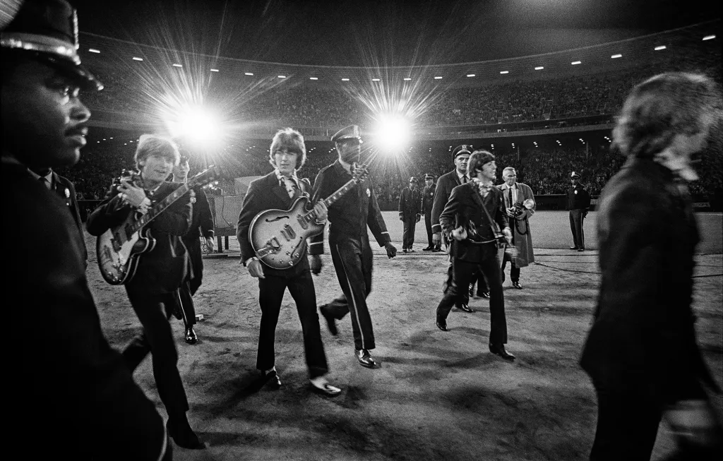 A photo of the Beatles walking across the baseball field to the stage.